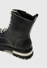 Melnas ādas potītes zābaki ar baltām auklām, ar biezu teksturētu zoli, sudraba akcentiem un kontrastējošiem šuvuma detaļām. Zips aizmugurē.