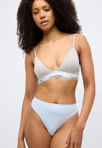 Γκρι μπραλέτα με λεπτές τιράντες και άσπρη λωρίδα Calvin Klein· σετ με ανοιχτόχρωμα μπλε σλιπ υψηλής μέσης με ανάγλυφο λογότυπο.