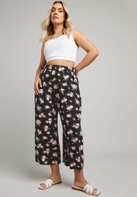 Pantaloni culotte neri a fiori con motivo di rose rosa, realizzati in tessuto leggero, abbinati a un top corto bianco e sandali bianchi.