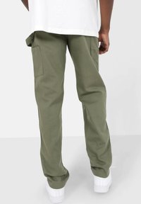 Oliven grøn cargo bukser med en afslappet pasform, der har sidelommer, en glat stoftekstur og tapered ankler, parret med hvide sneaks.
