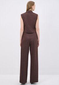 Brown mouwloze blazer gecombineerd met bijpassende wijde broek. De stof heeft een subtiele textuur en een strakke, op maat gemaakte silhoet.