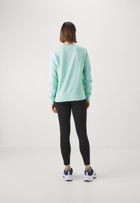 Jasno miętowy sweter z długimi rękawami, ściągaczami przy mankietach i u dołu, w połączeniu z czarnymi legginsami i białymi sneakersami na jednolitym tle.