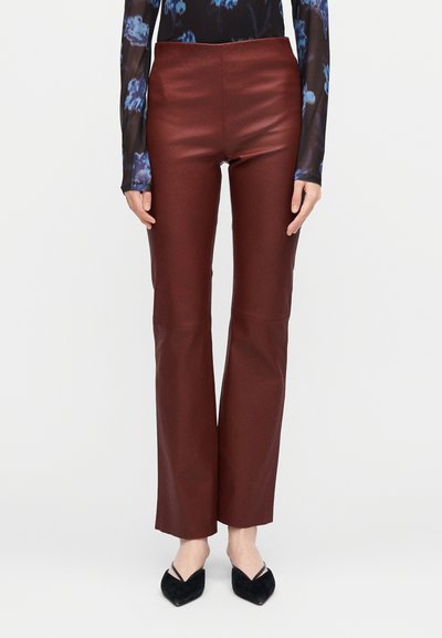 Brown fitted pants with a glossy texture, flared shape, high waist, and subtle seam detailing, paired with black pointed shoes.