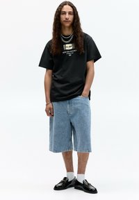 Sort bomulds t-shirt med grafisk tryk, lyseblå denim shorts med snoet mønster og sorte loafers med hvide sokker. Sølv kædetrøjer.
