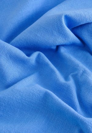 Gestructureerde blauwe linnen stof met zachte plooien en een subtiele glans, wat duidt op een lichtgewicht materiaal en een glad oppervlak.