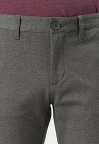 Pantalones gris texturizados con cierre de botón y bolsillos frontales, presentados en un modelo que lleva una camisa burdeos con un patrón sutil.