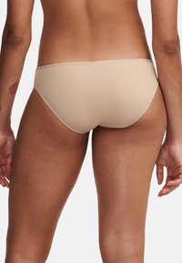 Beige Bikini-Slips aus einem glatten, weichen Stoff mit mittlerem Schnitt, die einfache Nähte entlang der Kanten aufweisen und keine sichtbaren Muster haben.