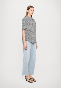 Black and white short-sleeve shirt with a spotted pattern, paired with light blue wide-leg jeans and black strappy heels.