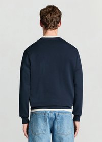 Sweat-shirt bleu marine avec poignets et ourlet côtelés, doté d'un col rond et d'un tissu texturé. Associé à un jean en denim bleu clair.