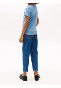 Modrá bavlněná tričko s krátkým rukávem, volný střih, spárované s vysokými modrými džínami. Hladká textura, jednoduchý design, minimální detaily.