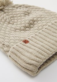 Berretto beige lavorato a maglia con motivo a diamante testurizzato e bordo a costine. Presenta una piccola etichetta in pelle marrone. Materiale morbido e caldo in misto lana.