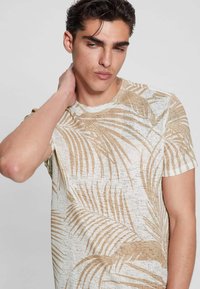 Kreminės spalvos trumpomis rankovėmis marškinėliai su tekstūriniu audiniu, kuriame yra auksinių delno lapų raštas; apvalios iškirptės dizainas, laisvas krovas.