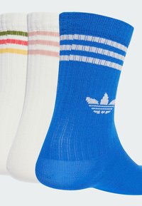 Tre paia di calze sportive: blu con strisce bianche e logo, bianche con strisce colorate, e motivi a strisce in verde, rosso e giallo.