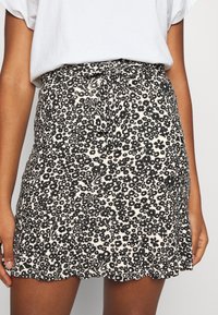 Zwarte bloemenprint minirok met een afgeronde zoom, gemaakt van lichtgewicht stof. Heeft een strikriem in de taille voor een verstelbare pasvorm.