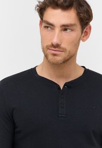 Schwarzes Langarm-Henley-Shirt aus strukturiertem Stoff, mit drei Knöpfen an der Knopfleiste und einem kleinen Logo-Akzent auf der Brust.