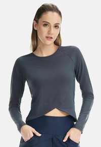 Long-sleeve athletic top in navy blue, featuring a crossover design at the hem and smooth fabric texture. Accented with a logo on the sleeve.