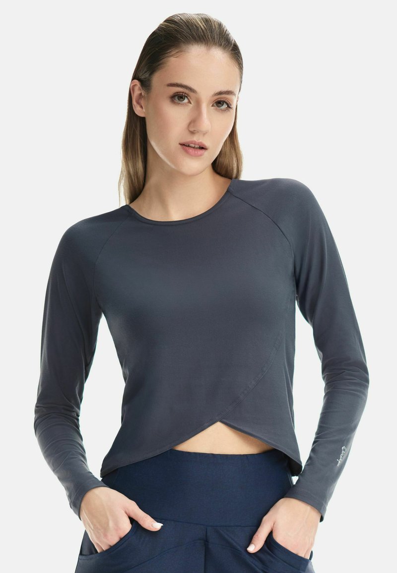 Long-sleeve athletic top in navy blue, featuring a crossover design at the hem and smooth fabric texture. Accented with a logo on the sleeve.
