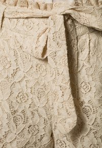 Krämfärgade spetsshorts med blommönster, volangmidja och knytband. Texturen är delikat och genomskinlig.