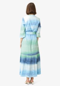 Rochie lungă, fluidă, cu un gradient de nuanțe de albastru și verde, confecționată dintr-un material ușor, cu mâneci tip clopot și tiv în mai multe straturi.