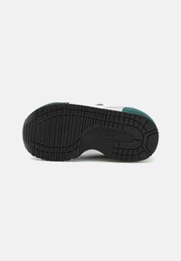 Semelle de sneaker en caoutchouc noir avec un motif de semelle texturé et des accents teal. Présente un upper blanc et un design de bout arrondi.