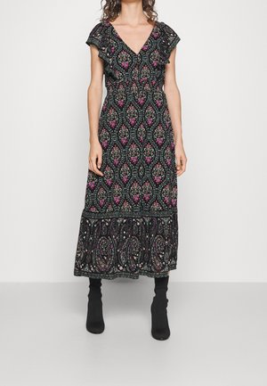Schwarz gemustertes Maxikleid mit Rüschensäumen, das bunte Blumen- und Paisleymuster zeigt. Tragen mit schwarzen Stiefeletten.