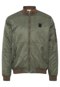 Olive green bomber jacket with a front zipper, ribbed collar, and cuffs. Features a pocket on the sleeve and a black logo patch. Waterproof material.