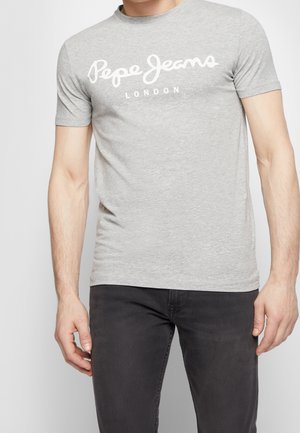 Mężczyzna ubrany w jasnoszarą koszulkę z krótkim rękawem z napisem "Pepe Jeans London" w białym stylu pisma oraz ciemnoszare jeansy na jednolitym tle.