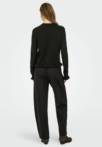 Pull vert foncé avec un ourlet en volants et des manches longues, associé à un pantalon noir ample et des bottines. Texture lisse.