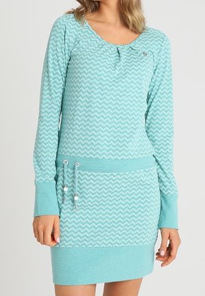 Woman wearing a long-sleeve, light blue chevron-patterned dress with drawstring waist and ribbed cuffs and hem.