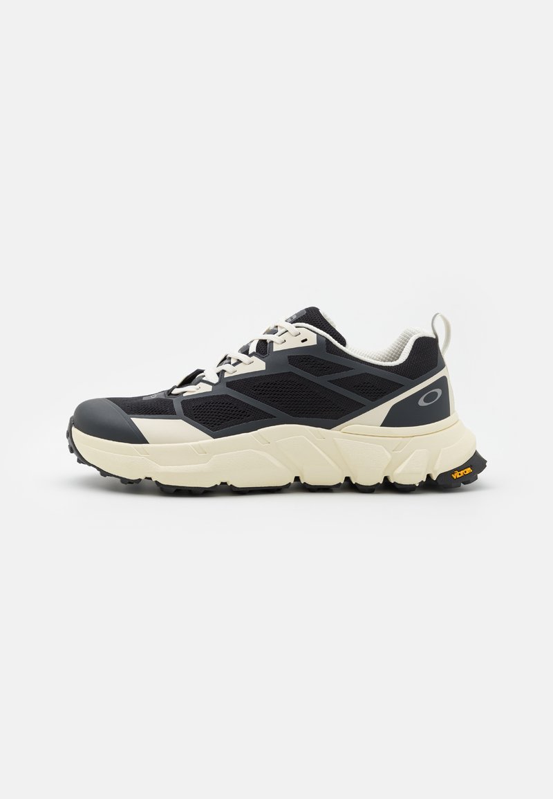 Sapato atlético preto e creme com parte superior em malha texturizada, sola de borracha, almofadado espesso e um destaque laranja "Vibram" na sola.