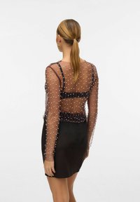Black mini dress with a sheer, embellished long-sleeve top featuring white bead details and a fitted waist. The back is slightly open.