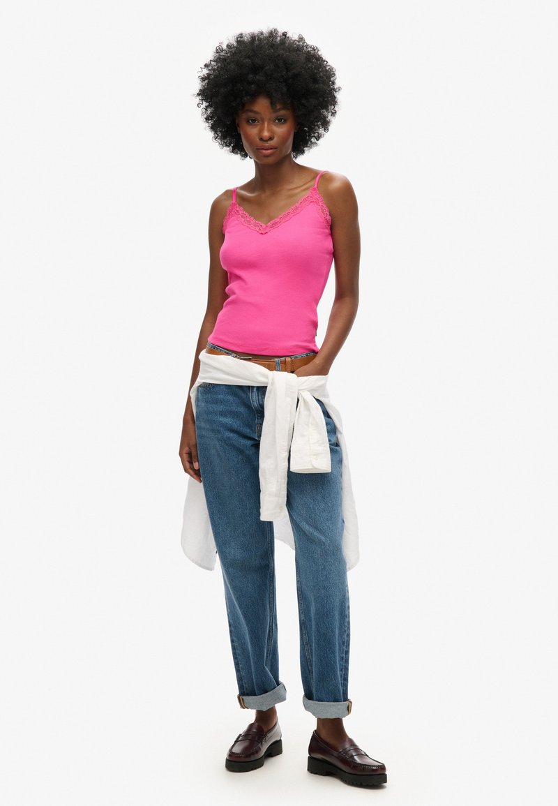 Camiseta de tirantes rosa con encaje, jeans azules holgados remangados en los puños, camisa blanca atada en la cintura y mocasines marrones.