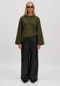 Gestreepte groene en zwarte long-sleeve top met brede mouwen, gecombineerd met losse zwarte neplederen broek en instap schoenen.