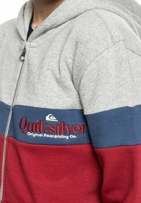 Felpa con zip grigia, blu e rossa con logo Quiksilver e testo "Original Boardriding Co." sul petto.