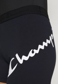 Czarne spodenki sportowe z miękkiego, elastycznego materiału. Posiadają szeroki czarny pas i wyraźne białe logo z boku.