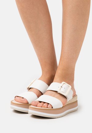 White wedge sandals with two wide straps and a buckle detail, featuring a textured platform sole in beige and a smooth white finish.
