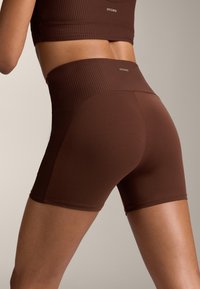 Barna bordázott, magas derekú rövidnadrág, rugalmas anyagból készült, sima textúrával és minimális logóval a derékrészen.