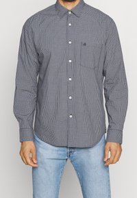 Långärmad skjorta med knappar framtill, i marinblått och vitt rutmönster, med bröstficka och rundad nederkant. Tillverkad av bomullsblandning.