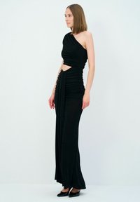 Czarna sukienka na jedno ramię z marszczonym wzorem, z wycięciem w środkowej części i długością do podłogi. Gładki materiał z eleganckim drapowaniem.