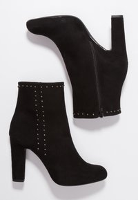 Botines de ante negros con un alto tacón bloque, acentuados con tachuelas metálicas a lo largo de los lados, con una cremallera lateral para el cierre.