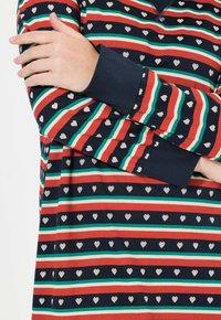 Maglietta a maniche lunghe blu navy con strisce orizzontali rosse, verdi e crema, intervallate da piccoli motivi a forma di cuore bianchi.