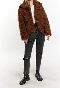 Brun faux fur frakke med krave, knaplukning, parret med slidte sorte jeans med frynset kant og hul på knæene, topped med sorte støvler.