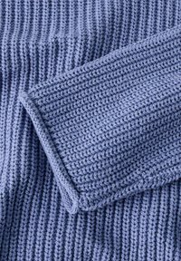 Tissu de pull en tricot bleu clair, présentant un motif côtelé texturé. Les manches sont repliées, mettant en valeur un bord lisse et une texture douce.