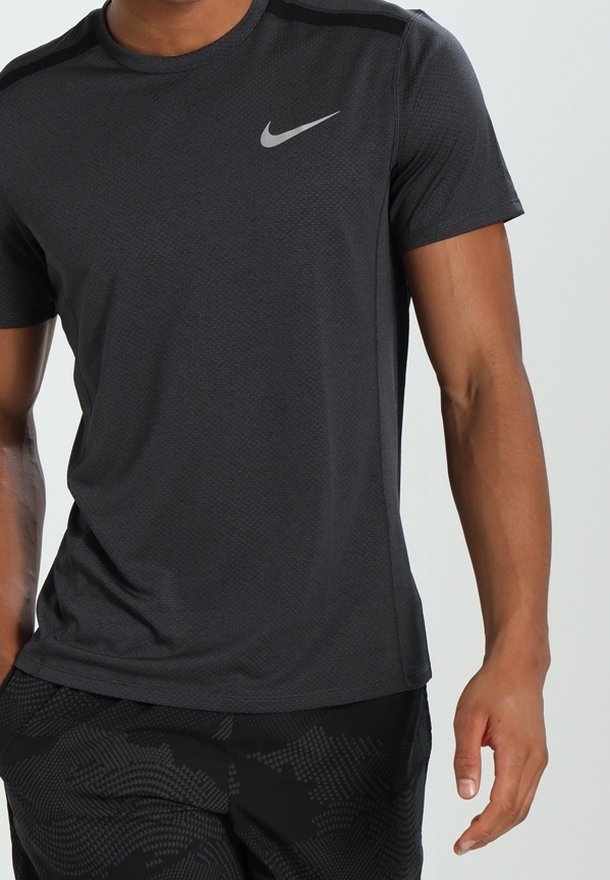 Mężczyzna ubrany w czarną koszulkę sportową Nike z krótkim rękawem oraz czarne spodenki w wzory, stojący z rękoma luźno wzdłuż ciała.