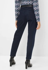 Marineblå højtaljede jeans med en tapered ben, udstyret med baglommer og et struktureret sort bælte, parret med en mønstret langærmet top.
