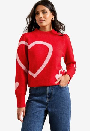 Roter Strickpullover mit großen rosa Herzmustern auf der Vorderseite und den Ärmeln. Rundhalsausschnitt, gerippte Bündchen und eine weiche Textur.