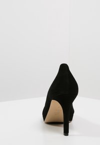 Black suede high-heeled shoe with a pointed toe and a slender heel, featuring a smooth texture and a minimalistic design.