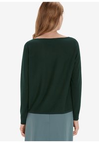 Top a maniche lunghe verde scuro con scollatura ampia. Texture liscia e vestibilità morbida, con orlo dritto, abbinato a una gonna azzurro chiaro.