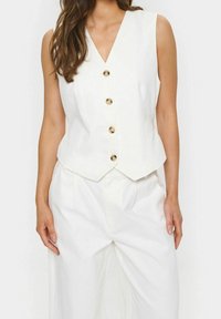 Vit linnerväst med V-ringning, med en skräddarsydd passform, fem stora krämfärgade knappar och en mjuk textur, i kombination med lösa vita byxor.
