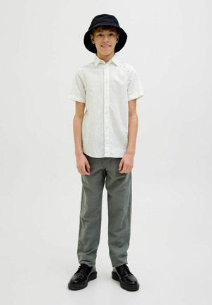 Camicia a maniche corte di colore chiaro, pantaloni grigi, cappello a secchiello nero e scarpe nere. Tessuto semplice con vestibilità rilassata.